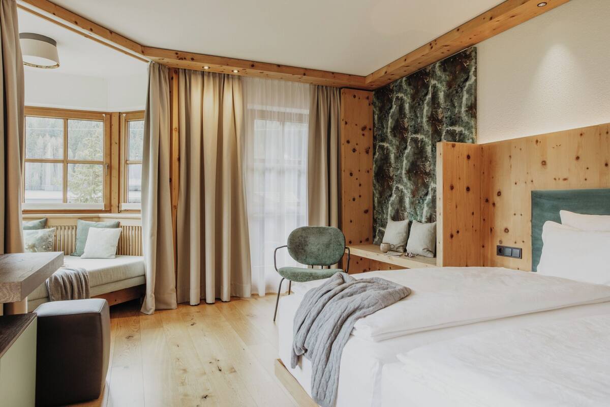 Un dormitorio con cama, una silla, un escritorio y una ventana con cortinas.