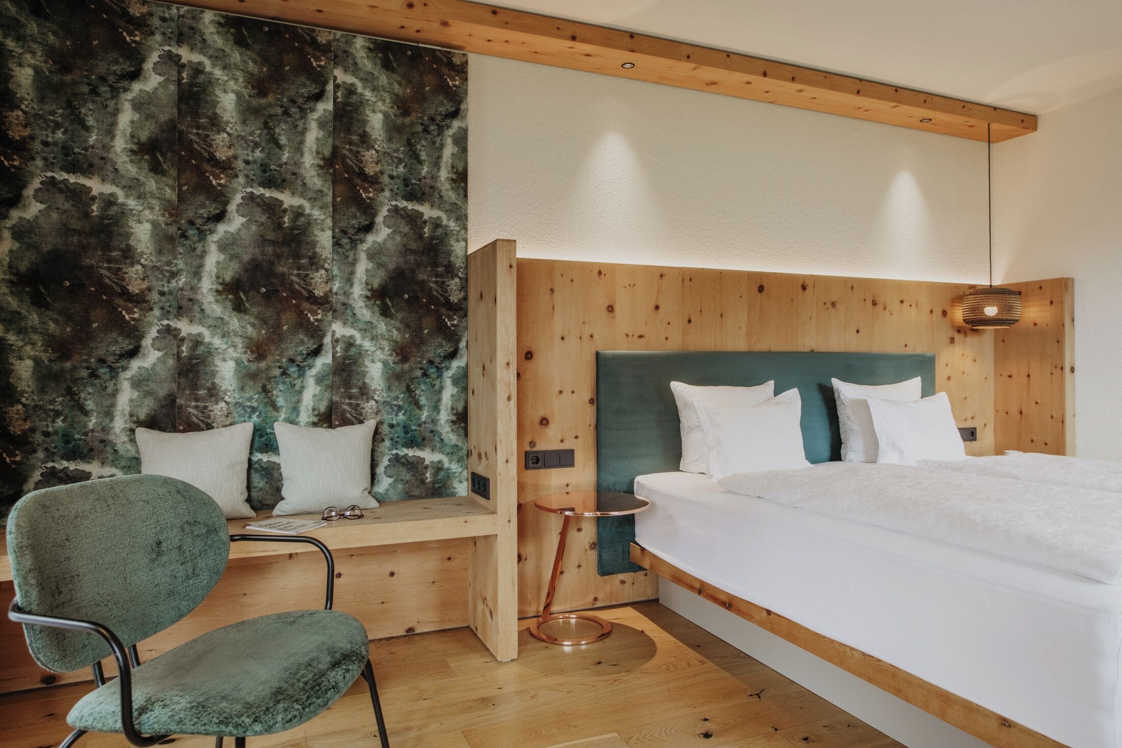Un dormitorio moderno con cabecera de madera, una butaca tapizada de verde y una mesita de noche.
