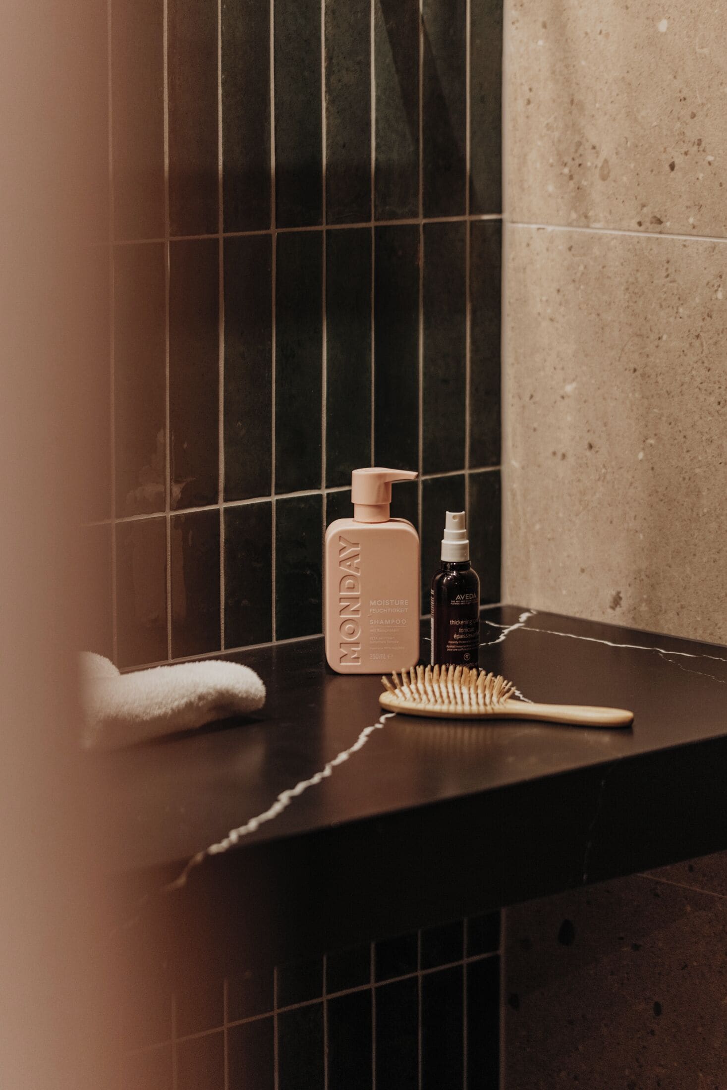 Una encimera de baño con una toalla, una botella de Champú Aveda Moisture y un cepillo de pelo.