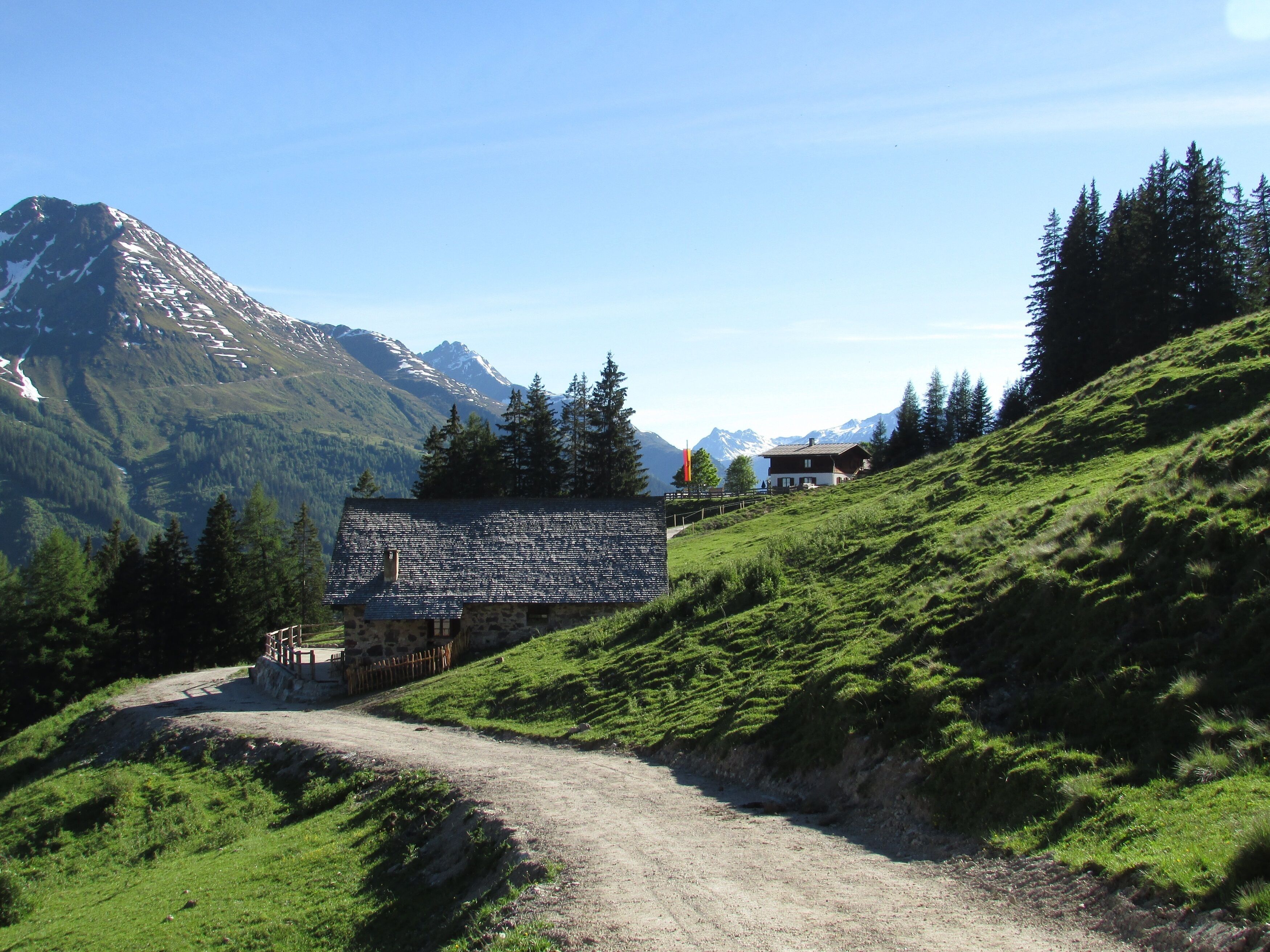 A stone building with a sloped roof, located on a hillside with a dirt path leading to it.