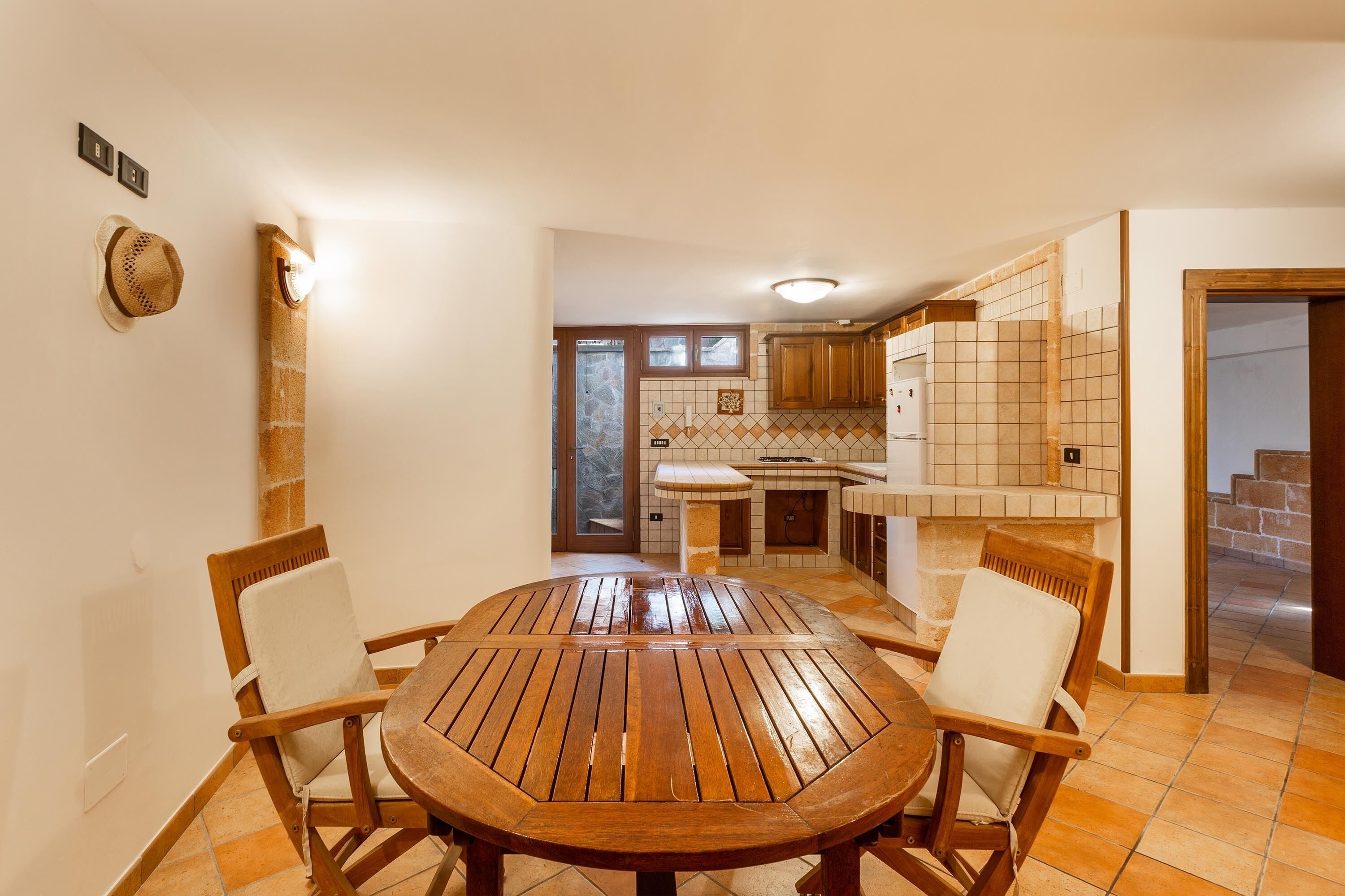 A dining area with a wooden table and chairs, a kitchen with tiled backsplash, and a stone wall.