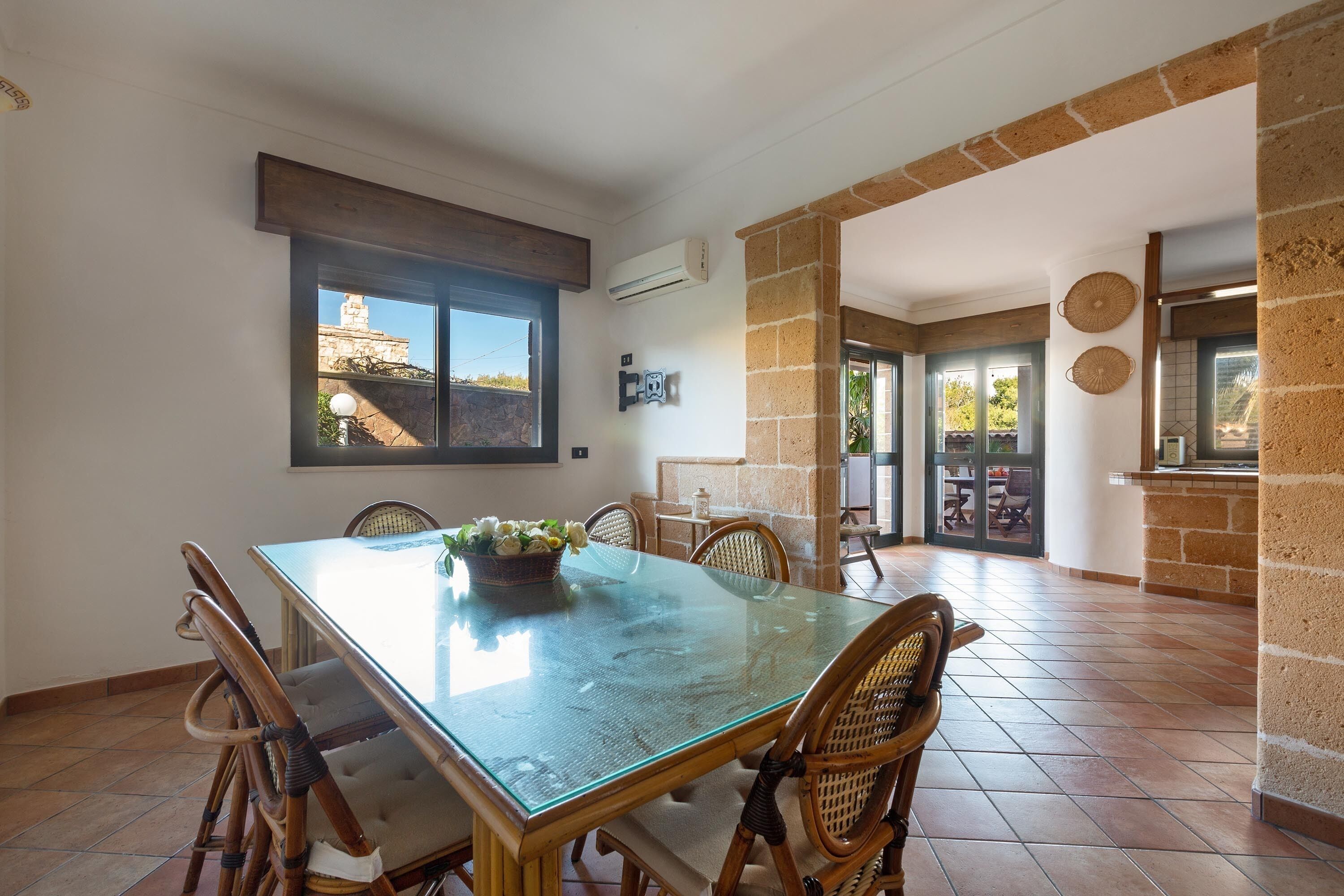 A dining area with a glass table, wicker chairs, and a view of a building through a window.