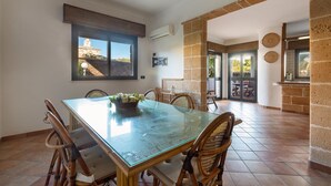 A dining area with a glass table, wicker chairs, and a view of a building through a window.