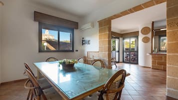 A dining area with a glass table, wicker chairs, and a view of a building through a window.