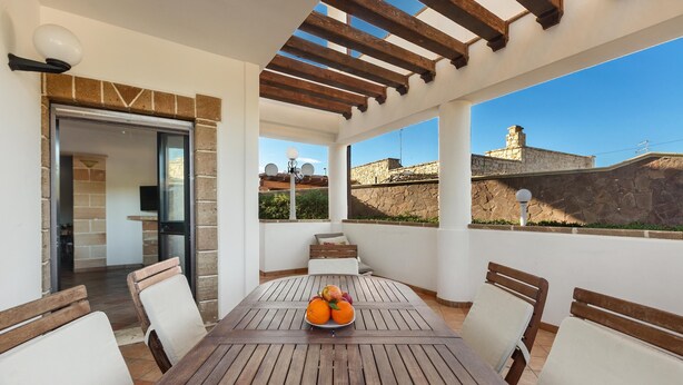 A patio with a wooden table and chairs, a bowl of fruit, and a view of the cityscape.