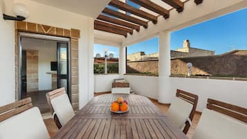 A patio with a wooden table and chairs, a bowl of fruit, and a view of the cityscape.