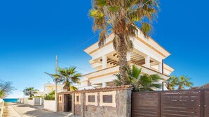 A two-story building with a balcony, surrounded by palm trees and a clear blue sky.