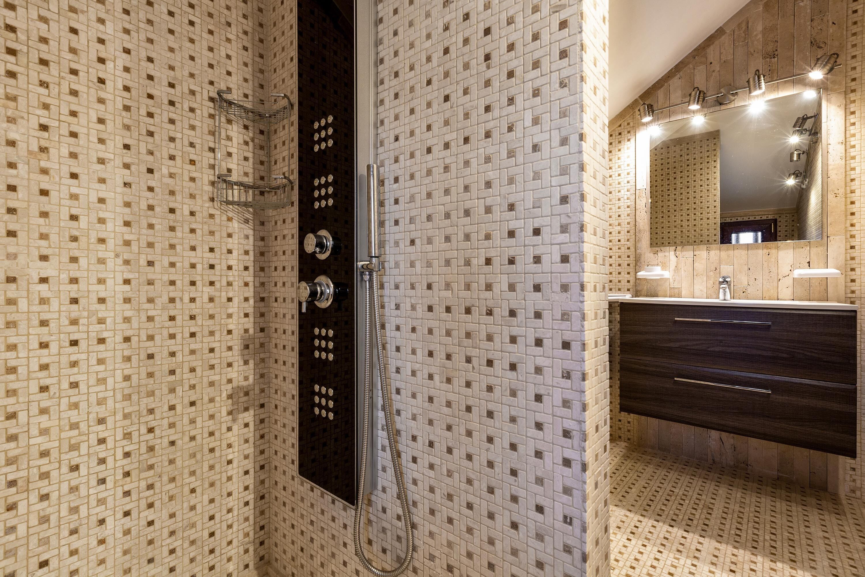 A bathroom with a tiled wall, a shower with a handheld showerhead, a dark wooden vanity with a mirror, and a sink.