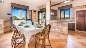 A dining area with a table set for four, surrounded by wicker chairs, a kitchen with a tiled backsplash, and a view through the open door. - 3218 Villa Eden - Primo Piano By Barbarhouse (Maruggio)