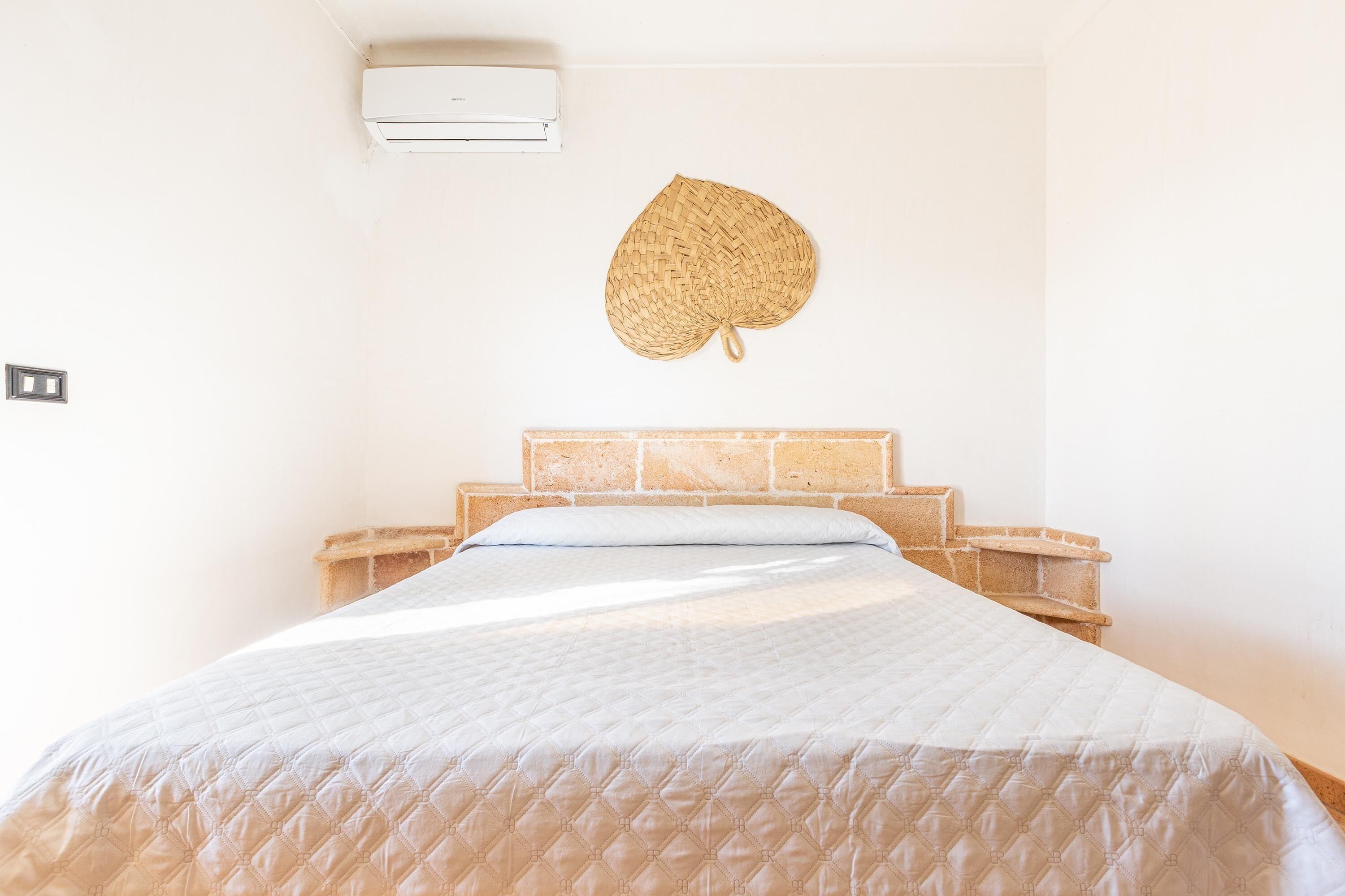 Un lit avec une couvre-lit matelassé, une tapisserie murale tissée et une tête de lit en pierre.