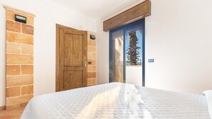 A bedroom with a bed, a wooden door, a stone wall, and a window with a view of a palm tree. - 3218 Villa Eden - Primo Piano By Barbarhouse (Maruggio)