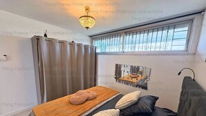 Een slaapkamer met een bed, een raam met gordijnen, een kroonluchter en een spiegel aan de muur.