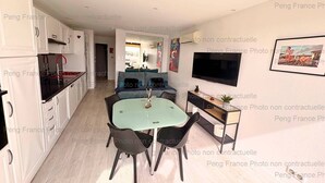 Een moderne keuken met witte kastjes, een zwarte aanrecht en een eethoek met een glazen tafel en zwarte stoelen.