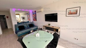 Een moderne woonkamer met een bank, een televisie en een eethoek met een tafel en stoelen.