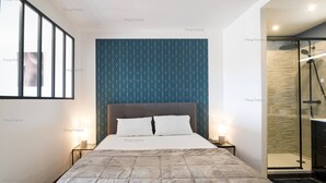 Habitación de hotel con cama, mesitas de noche, zona de ducha y ventana.
