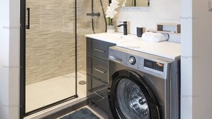 Un baño moderno con cabina de ducha de vidrio, lavadora y espejo.
