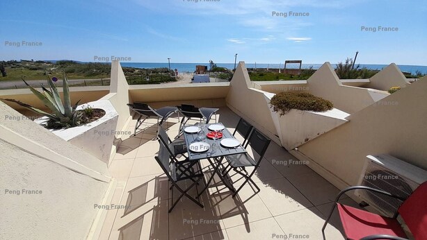 Une terrasse extérieure avec une table dressée pour deux personnes, entourée de chaises, et donnant sur une plage.