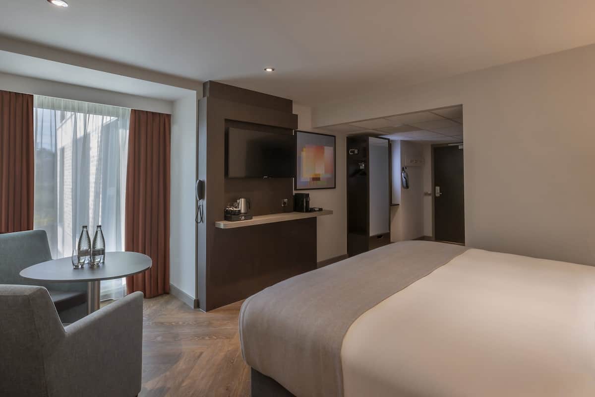 Ein Hotelzimmer mit Bett, Schreibtisch, Stuhl, Fernseher und einem Fenster mit Vorhängen.