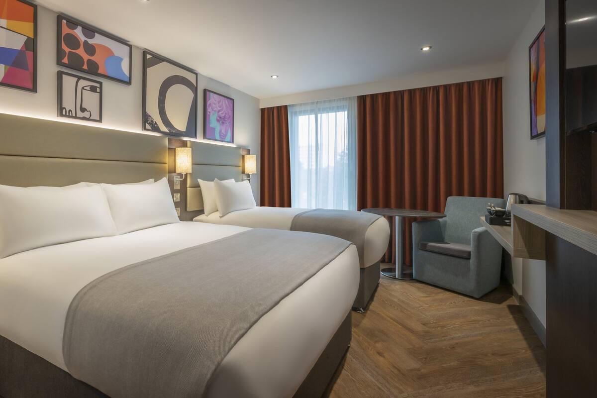 Ein Hotelzimmer mit zwei Betten, einem Schreibtisch, einem Sessel und Bildern an den Wänden.