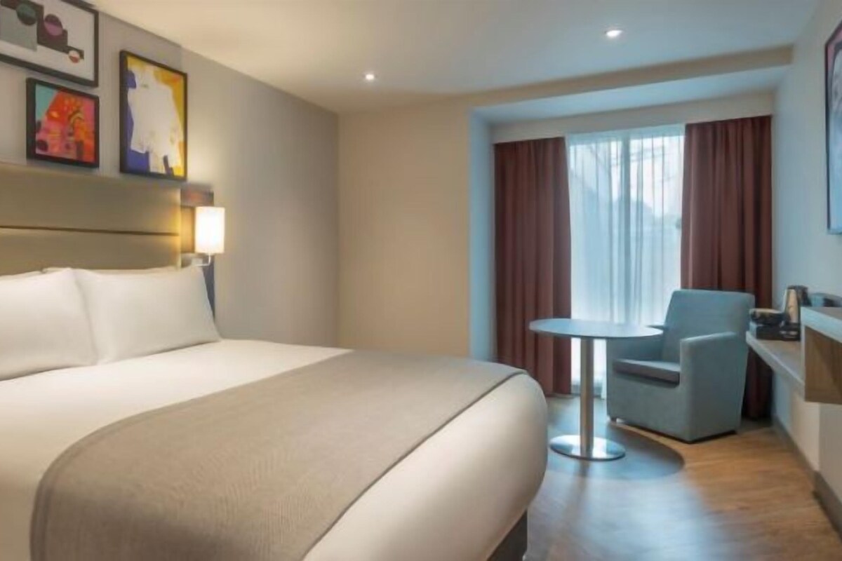 A hotel room with a large bed, a small table, a chair, and a TV.