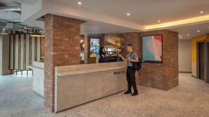 Un área de recepción con un pilar de ladrillo, un mostrador de recepción que dice "RECEPTION" y un cuadro abstracto grande en la pared.