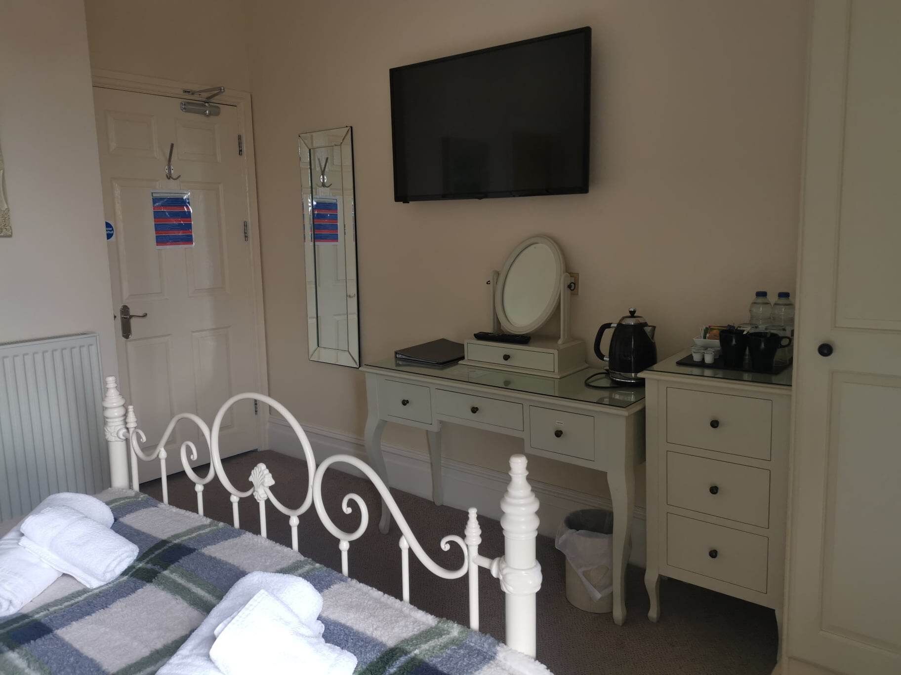 Une chambre à coucher comprenant un lit, une commode, un miroir, un téléviseur et un radiateur.
