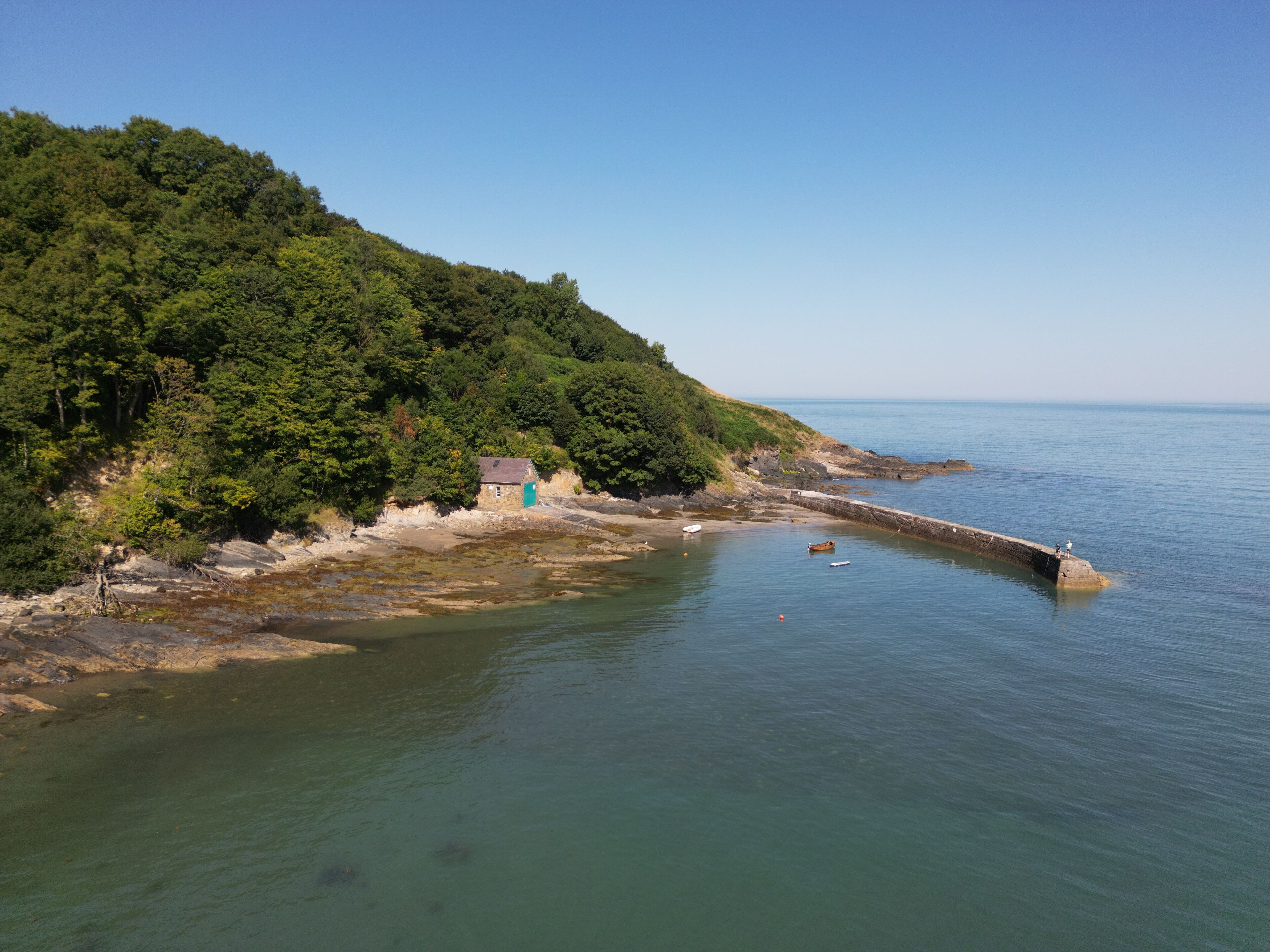 A coastal scene with a small house on a cliff, a rocky shoreline, and calm sea.