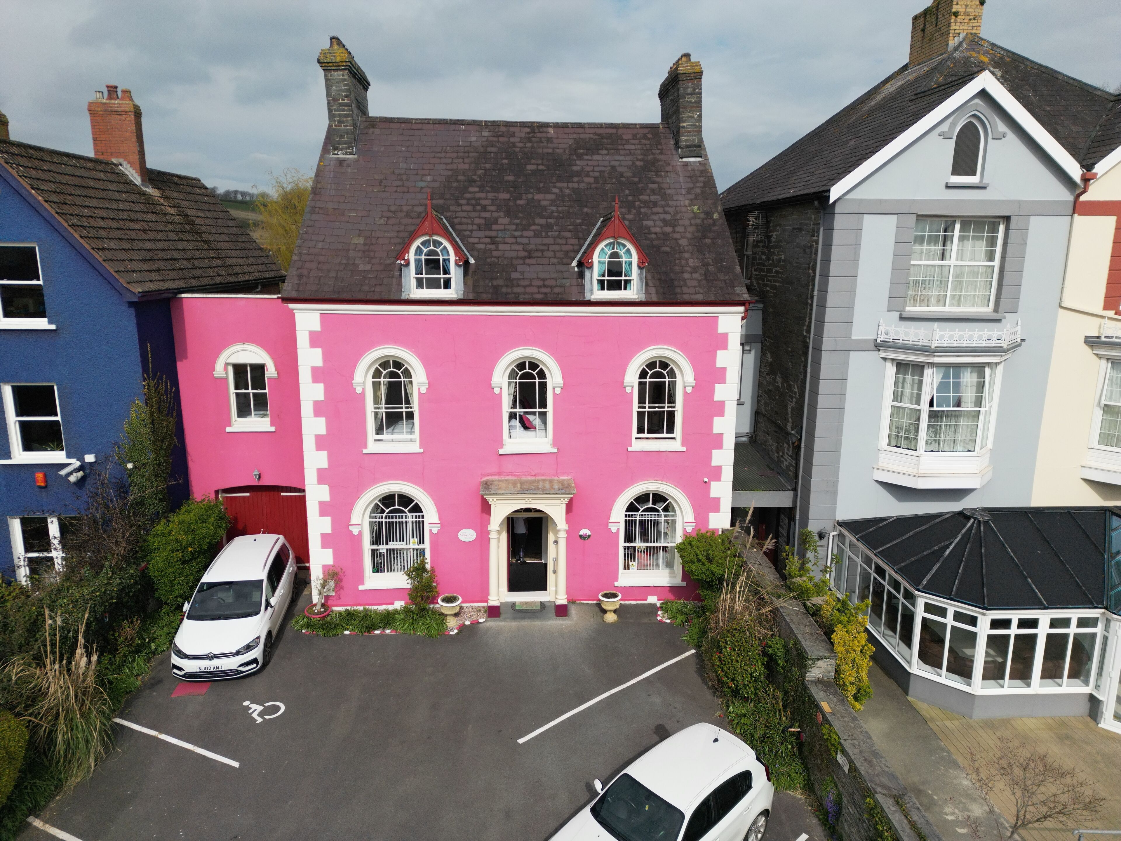Une maison rose avec un toit noir, des fenêtres blanches et une porte d’entrée.
