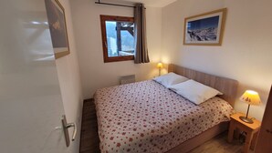 Un dormitorio con cama, ventana con cortinas, un cuadro en la pared, lámpara de noche y radiador.
