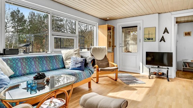 A modern living room with a large window, a sofa, a chair, a TV, and a bookshelf. - 3 bedroom amazing home in Glesborg (Glesborg)