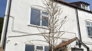 A two-story white building with multiple windows, a visible chimney, and a small garden area with outdoor furniture. - Hideaway (Whitby)