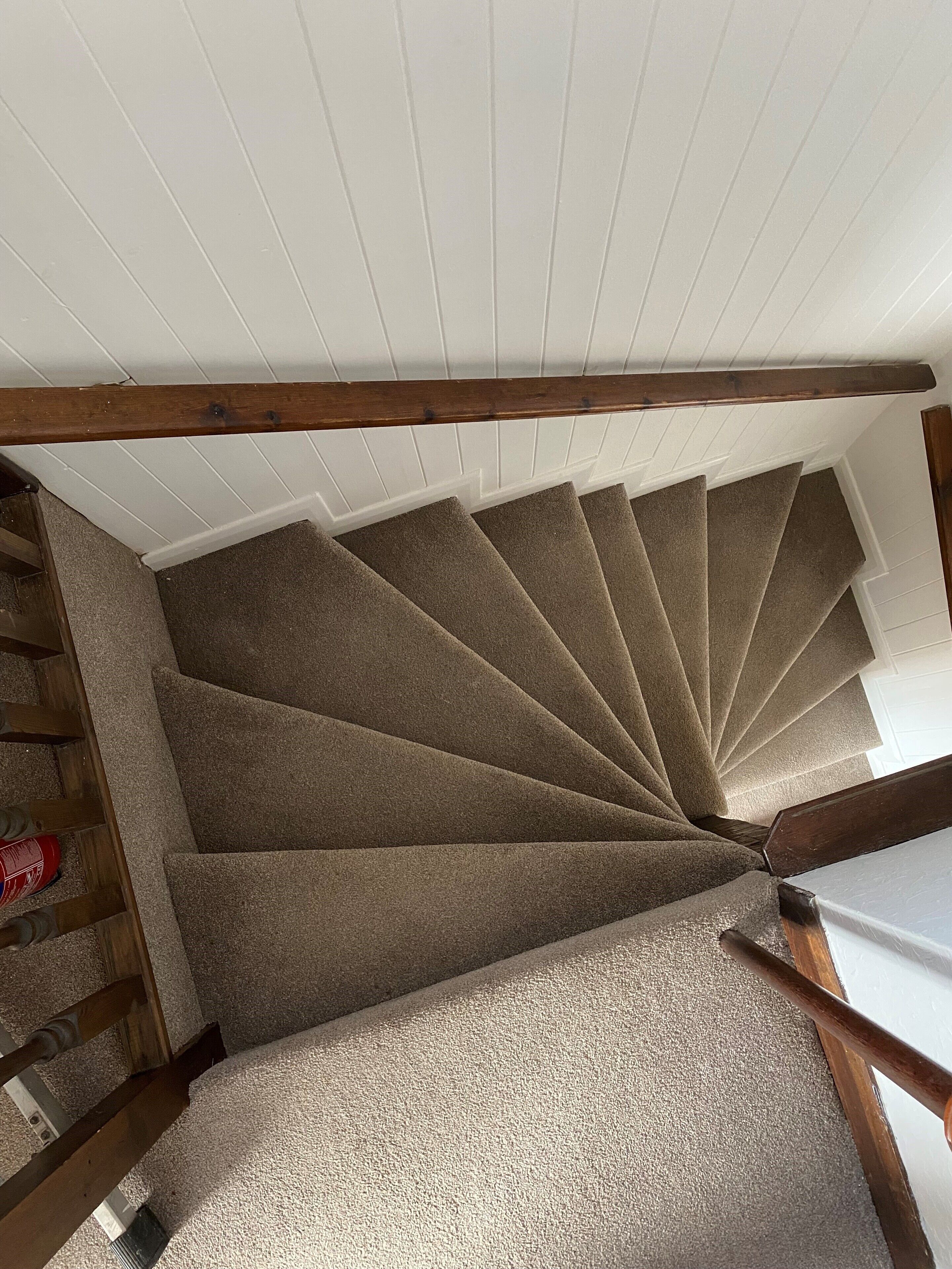 Eine Wendeltreppe mit beigefarbenen Teppichstufen, die zu einer weißen Tür führt.