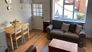 A cozy living room with a wooden dining table, a sofa, and a window with a view of a brick building. - Hideaway (Whitby)