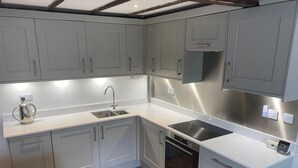A modern kitchen with grey cabinets, a stainless steel sink, a built-in oven, and a coffee maker. - Hideaway (Whitby)