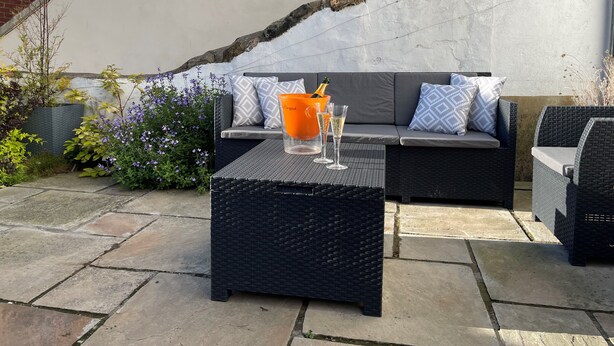 An outdoor seating area with a sofa and two chairs, a table with drinks, and a potted plant. - Hideaway (Whitby)