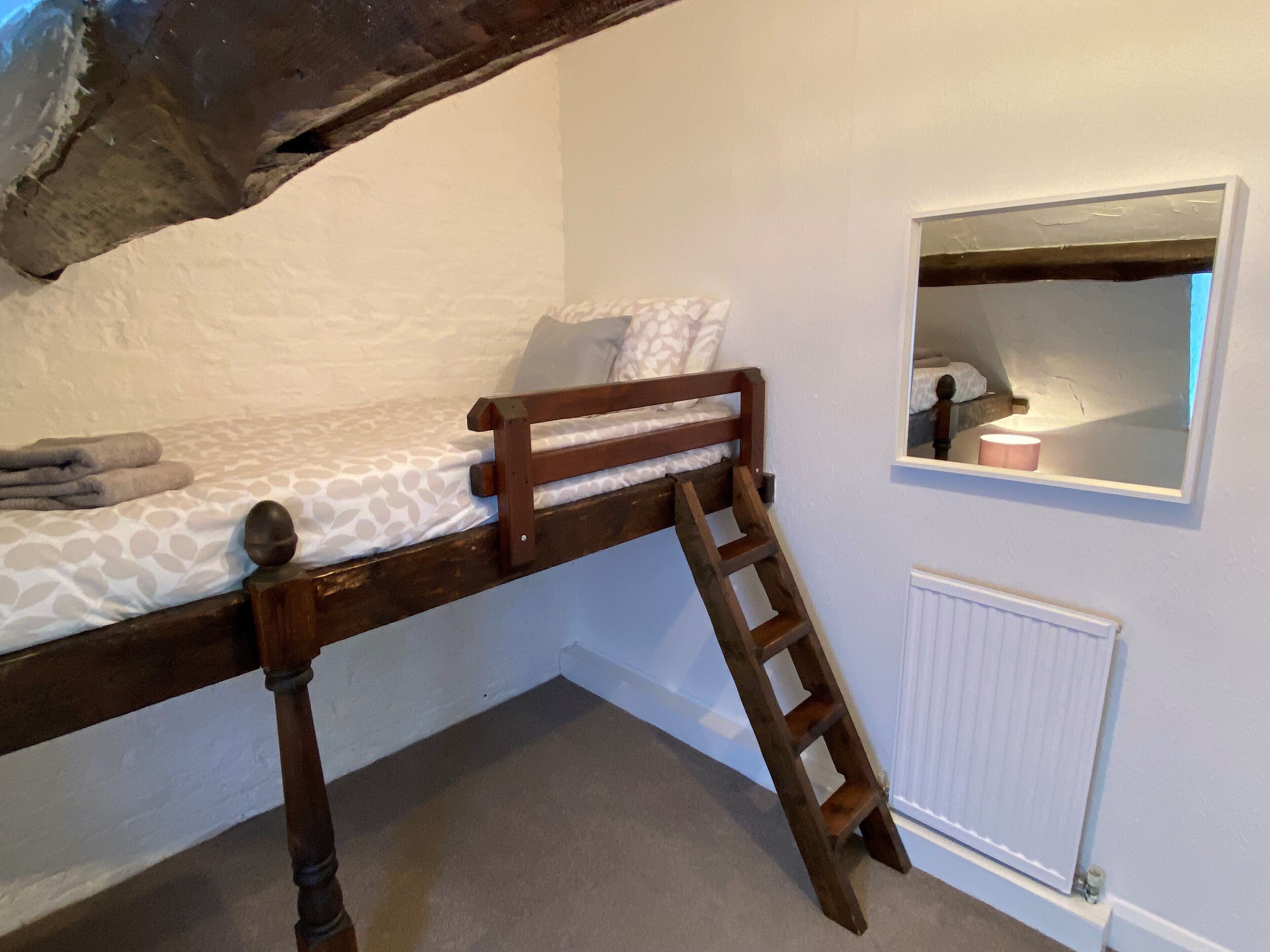 Un letto a castello con una scala in legno, una piccola finestra con uno specchio e un termosifone sulla parete.