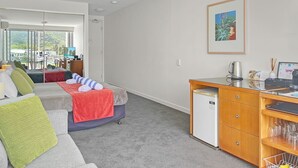 A modern hotel room with a sofa, a small desk, a refrigerator, and a view of the outdoors.