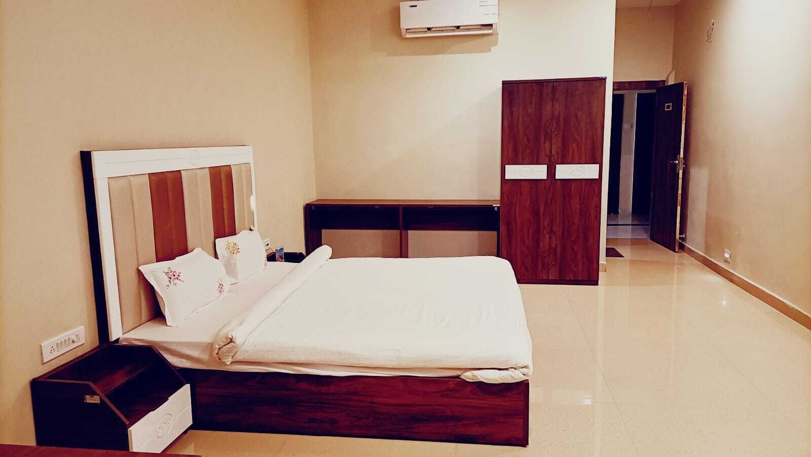 A hotel room with a bed, bedside table, wardrobe, and an air conditioning unit.