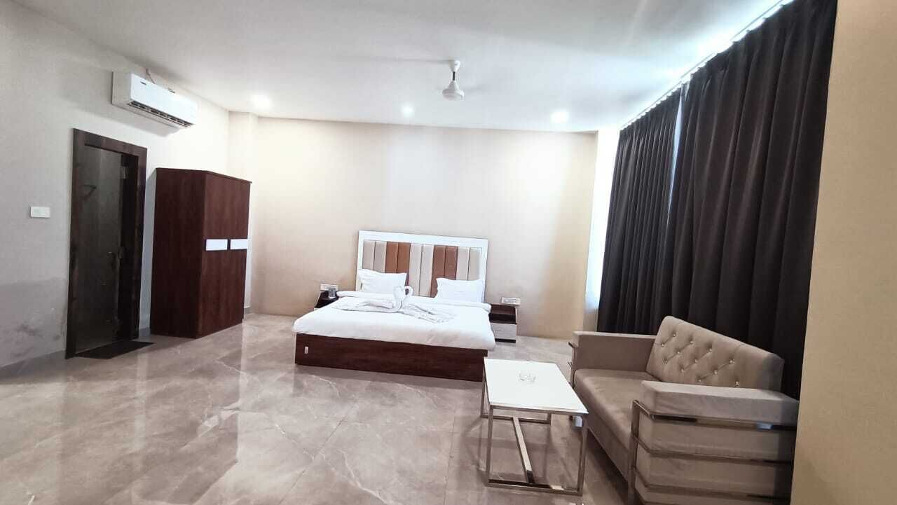 Habitación de hotel con cama, sofá, una mesita, armario y ventana con cortinas.
