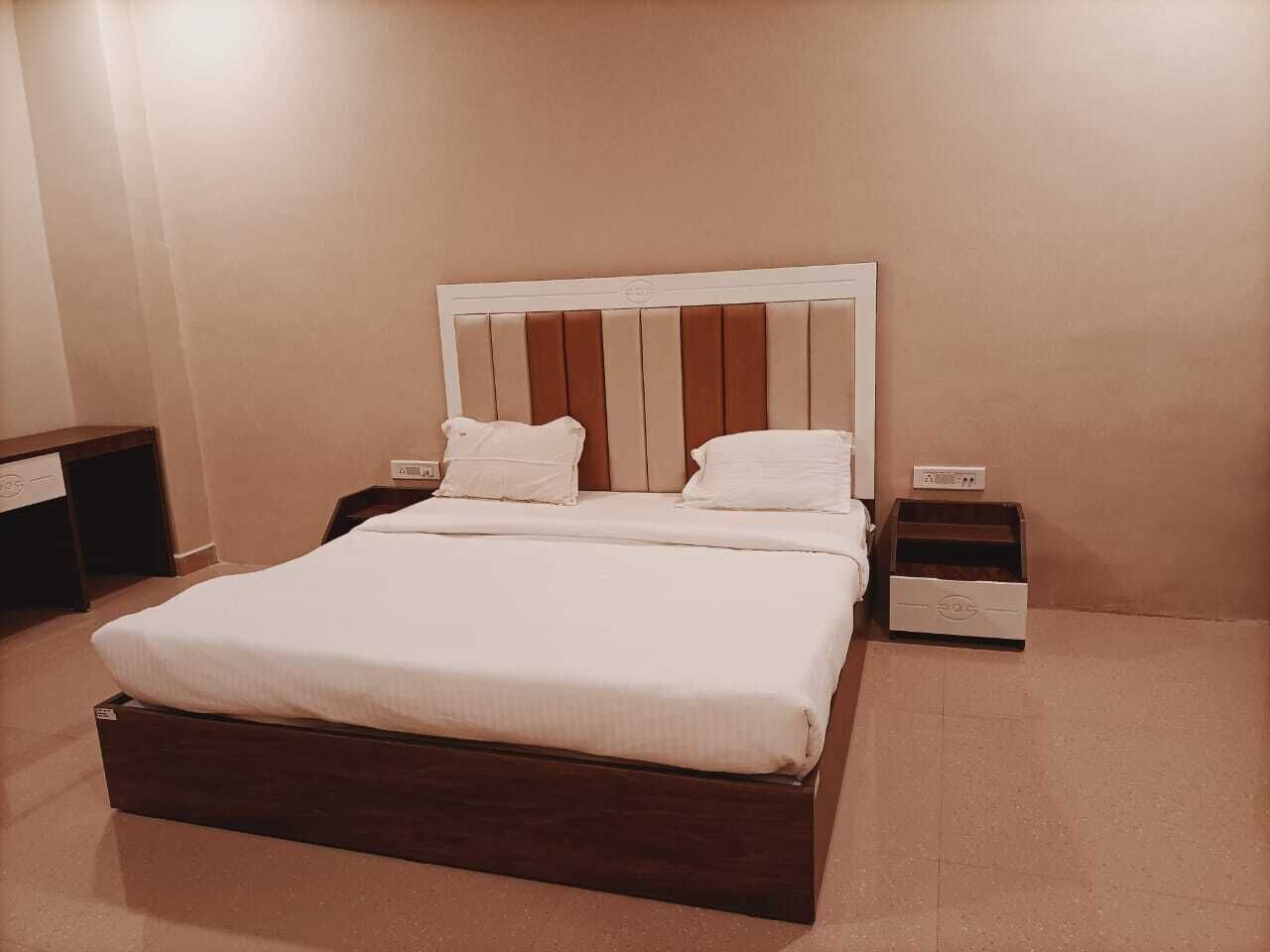 Un lit bien fait, avec un cadre en bois et une literie blanche, une table de chevet avec une lampe, et une petite commode placée à côté du lit.