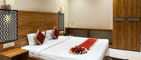 Een moderne hotelkamer met een houten bed, witte lakens, een rode decoratieve kussen, een nachtkastje, een luchtverfrisser aan de muur en een plafondventilator.