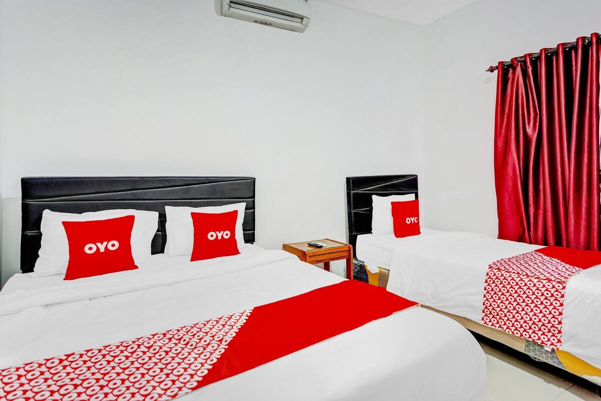 A hotel room with two beds, each with white bedding and red accents, including pillows and a blanket.