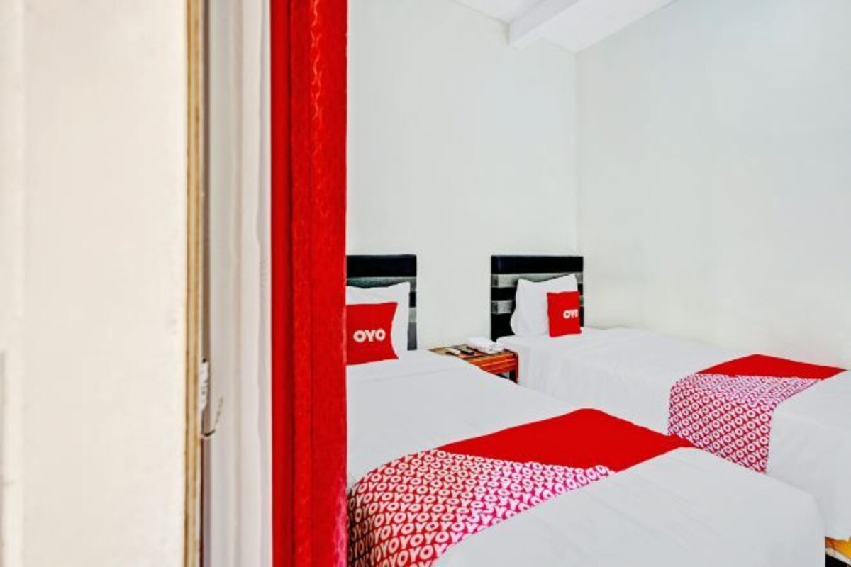 Habitación de hotel con dos camas, cada una con una colcha y almohadas de estampado rojo y blanco, y una cortina roja visible en parte.