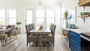 A modern kitchen with a dining area, featuring a wooden table, wicker chairs, and a hanging light fixture.