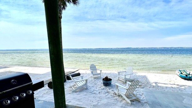 A beachside patio with a grill, lounge chairs, and a view of the ocean.