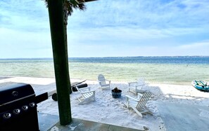 A beachside patio with a grill, lounge chairs, and a view of the ocean.