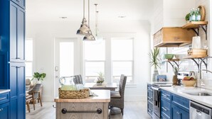 A modern kitchen with blue cabinets, a wooden island, and a dining area with a view.