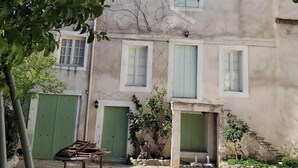 A courtyard with a gravel ground, a table with chairs, and a building with green shutters and a tiled roof. - Grand old Villa with pool in the heart  of  Capestang town (on the Canal du Midi) (Capestang)
