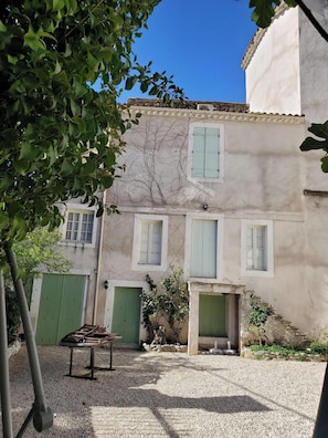 A courtyard with a gravel ground, a table with chairs, and a building with green shutters and a tiled roof. - Grand old Villa with pool in the heart  of  Capestang town (on the Canal du Midi) (Capestang)