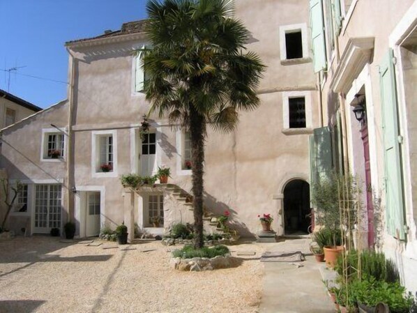 A courtyard with a palm tree, potted plants, and a building with a stone facade. - Grand old Villa with pool in the heart  of  Capestang town (on the Canal du Midi) (Capestang)